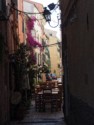 Narrow street filled with bougainvillea and tables