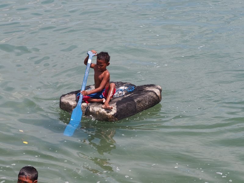 A little kid paddles from a piece of styrofoam