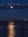 The moon reflects off the water and peeks through the Bay Bridge
