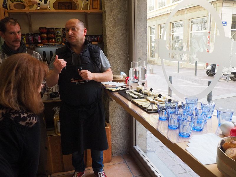 The shop owner explains French cheeses